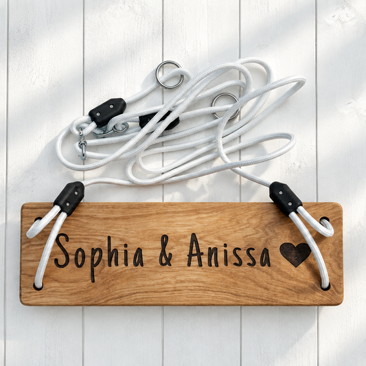 Personalized wooden name plaque hanging on a white wood plank wall, with white jump ropes and black-and-white handles draped above it. The plaque is engraved with the names 'Sophia & Anissa' and a small heart.