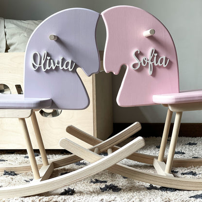 Two children's rocking horses, one pink and one purple, with names 'Olivia' and 'Sofia' on a neutral background.