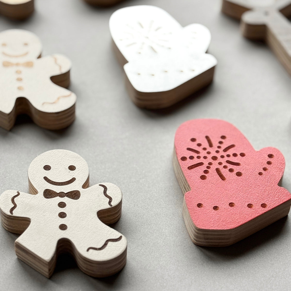 Wooden Christmas ornaments including gingerbread men and a mitten on a gray surface