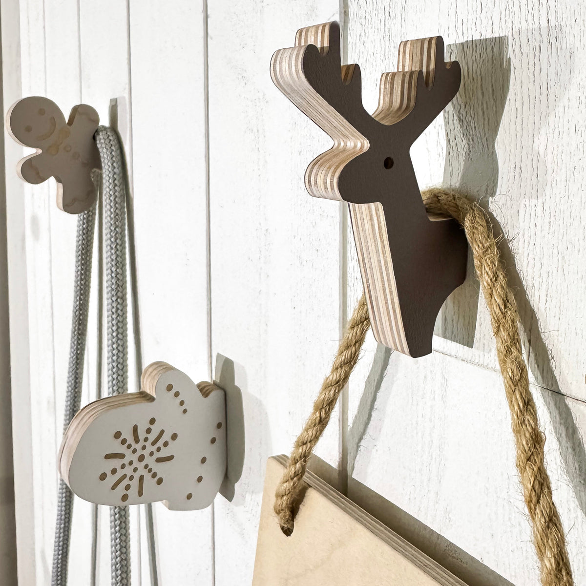 Decorative hooks shaped like a gingerbread man, snowflake, and reindeer on a wooden wall.