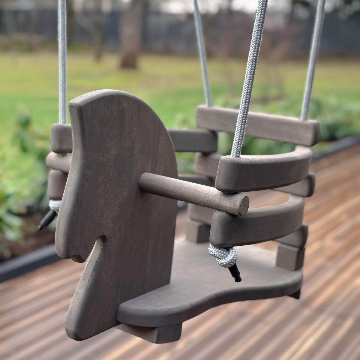 Children's swing with a wooden seat and metal ropes on a wooden deck.