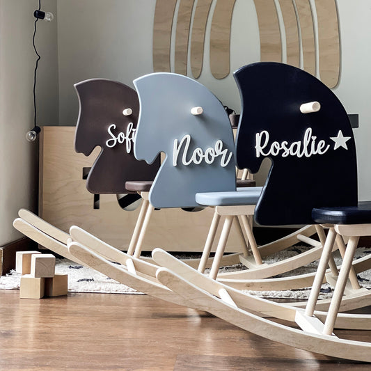 Three rocking horses with personalized names on a wooden floor.