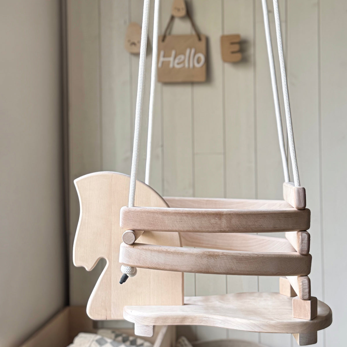 Wooden swing hanging against a light-colored wall with a 'Hello' sign.