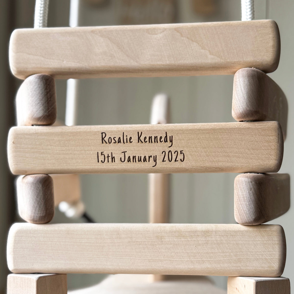 Wooden baby swing with engraved text on a blurred background