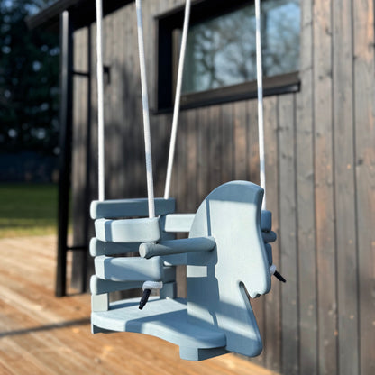 Child's swing set on a wooden deck with a modern house in the background