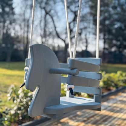 Wooden swing shaped like a horse in an outdoor setting with trees and grass.
