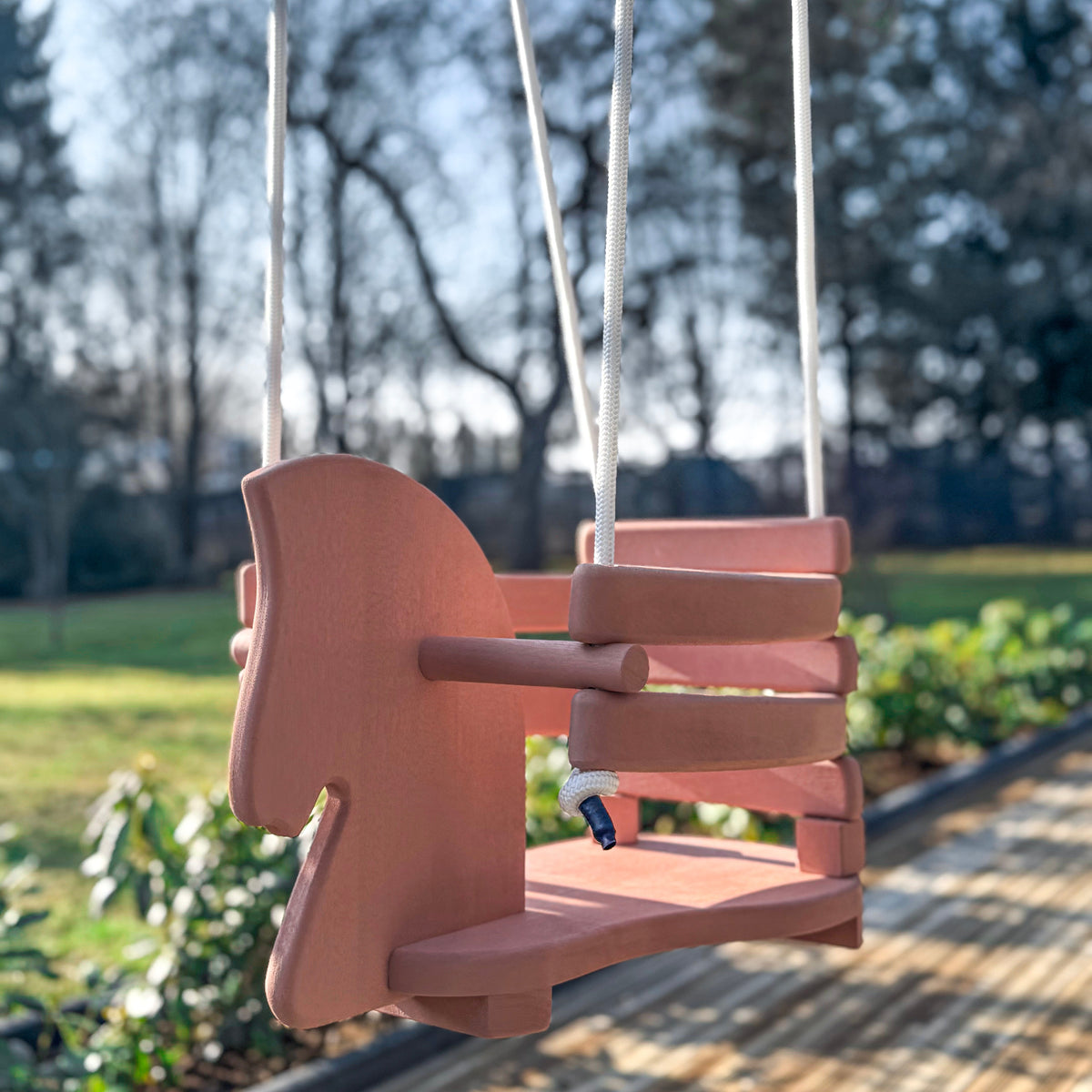Pink wooden swing set in a park with trees and grass in the background