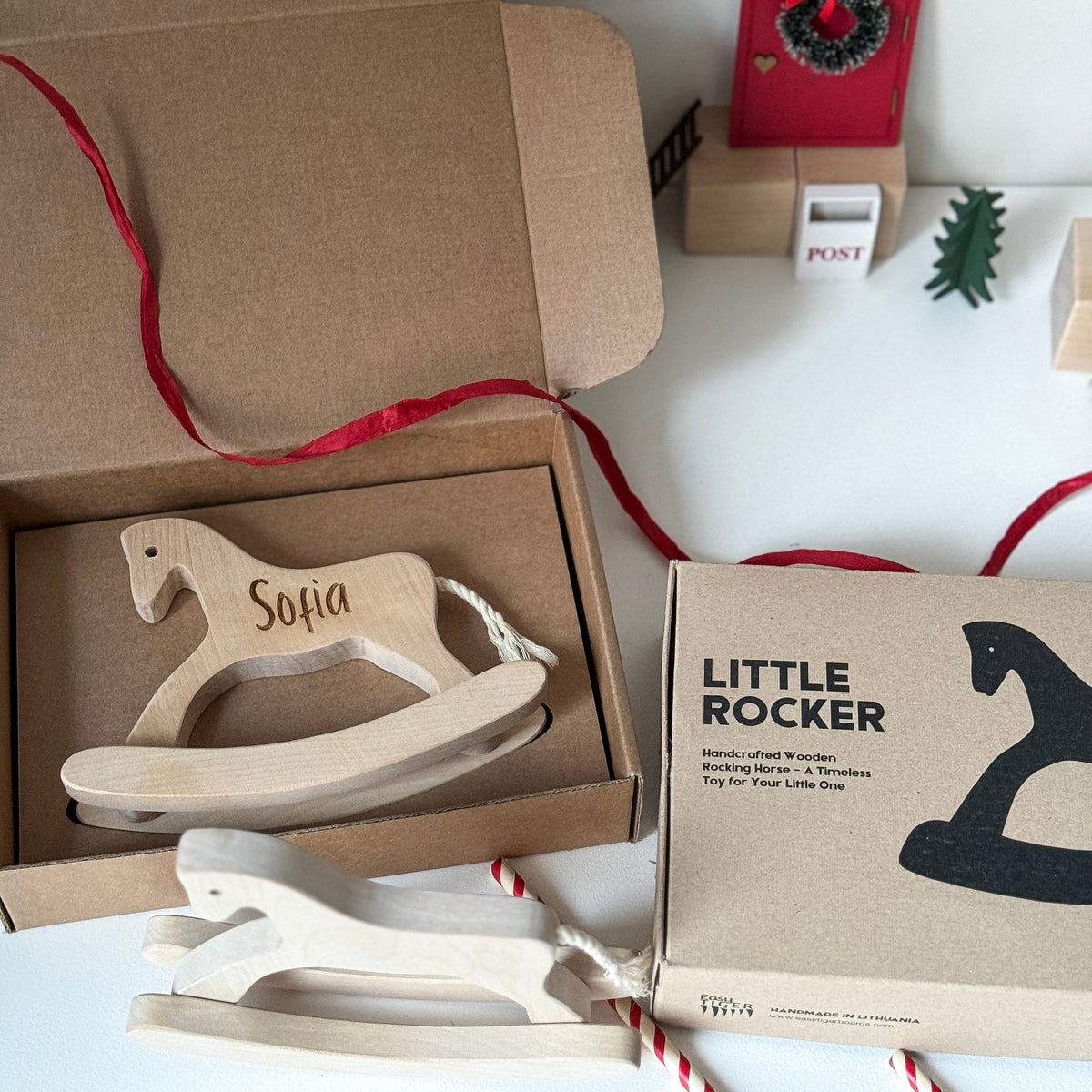 Wooden toy rocker with 'Sofia' engraving in a brown box, surrounded by festive decor.