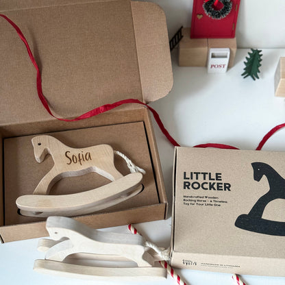 Wooden toy rocker with 'Sofia' engraving in a brown box, surrounded by festive decor.
