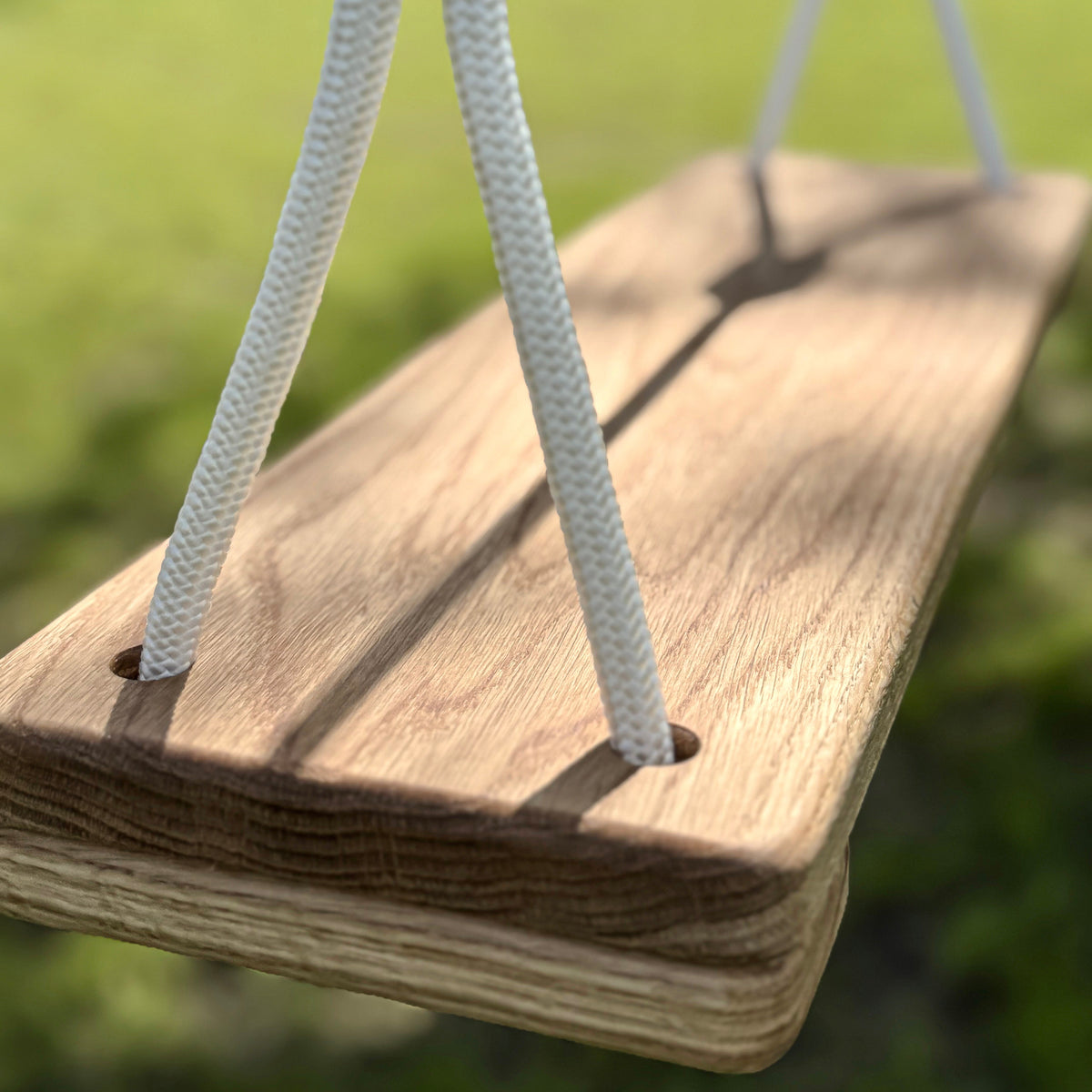 Wooden swing seat with a rope on a blurred green background