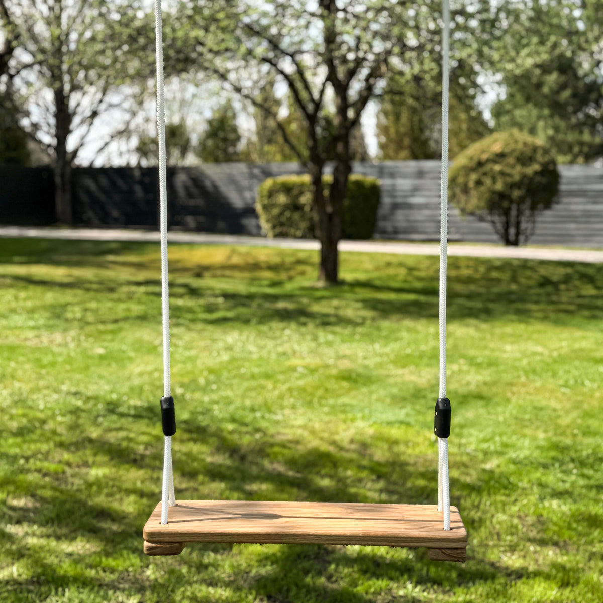 Wooden swing hanging on ropes in a grassy outdoor area with trees in the background