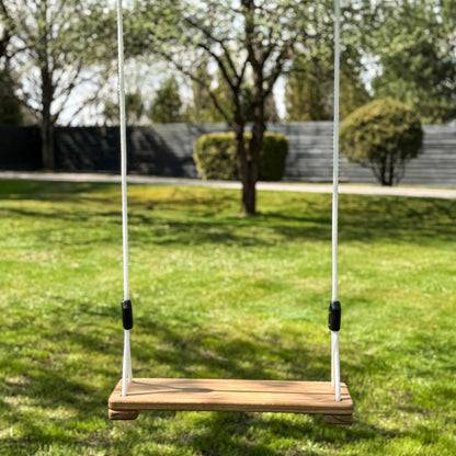 Wooden swing hanging on ropes in a grassy outdoor area with trees in the background