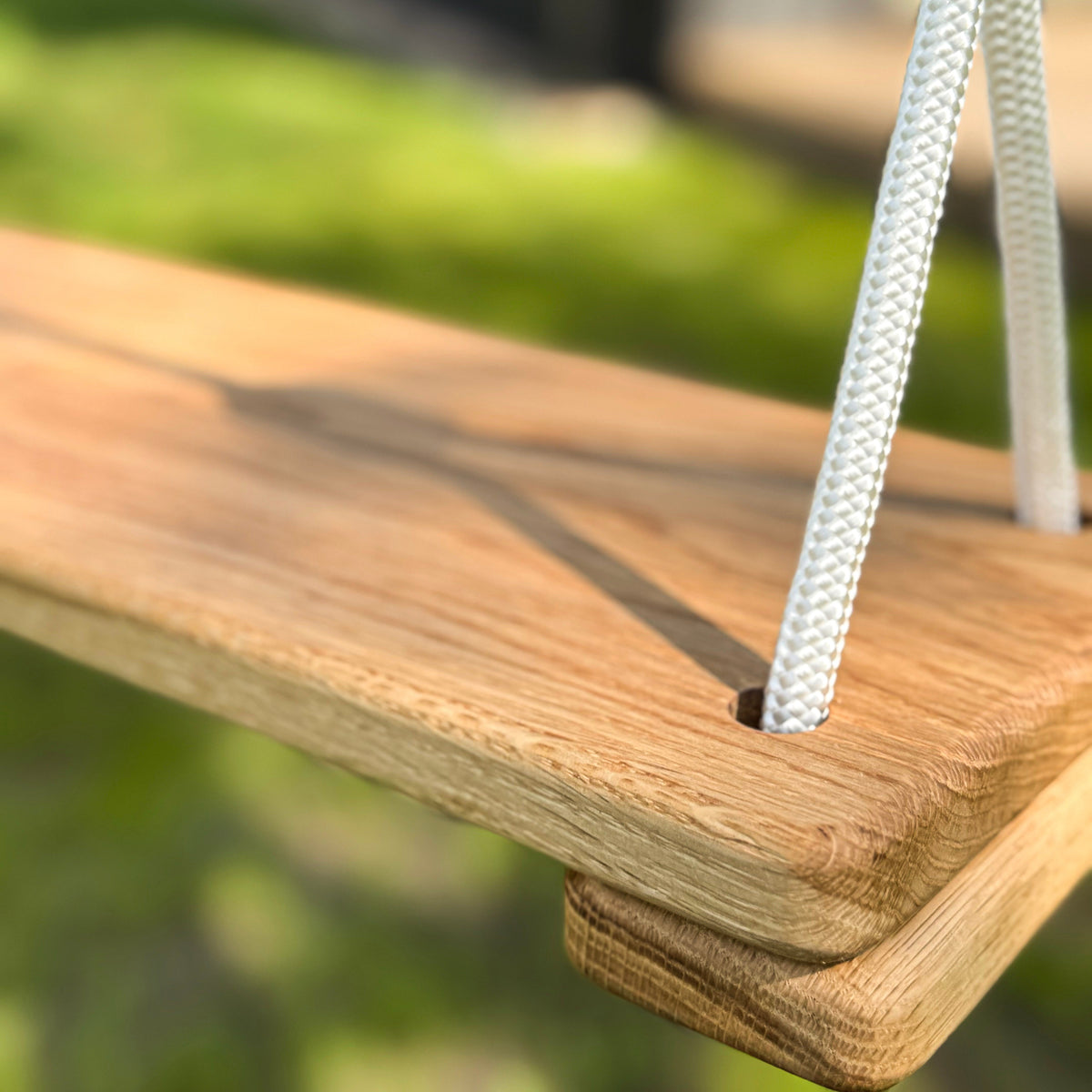 Wooden swing seat with a rope attachment against a blurred green background