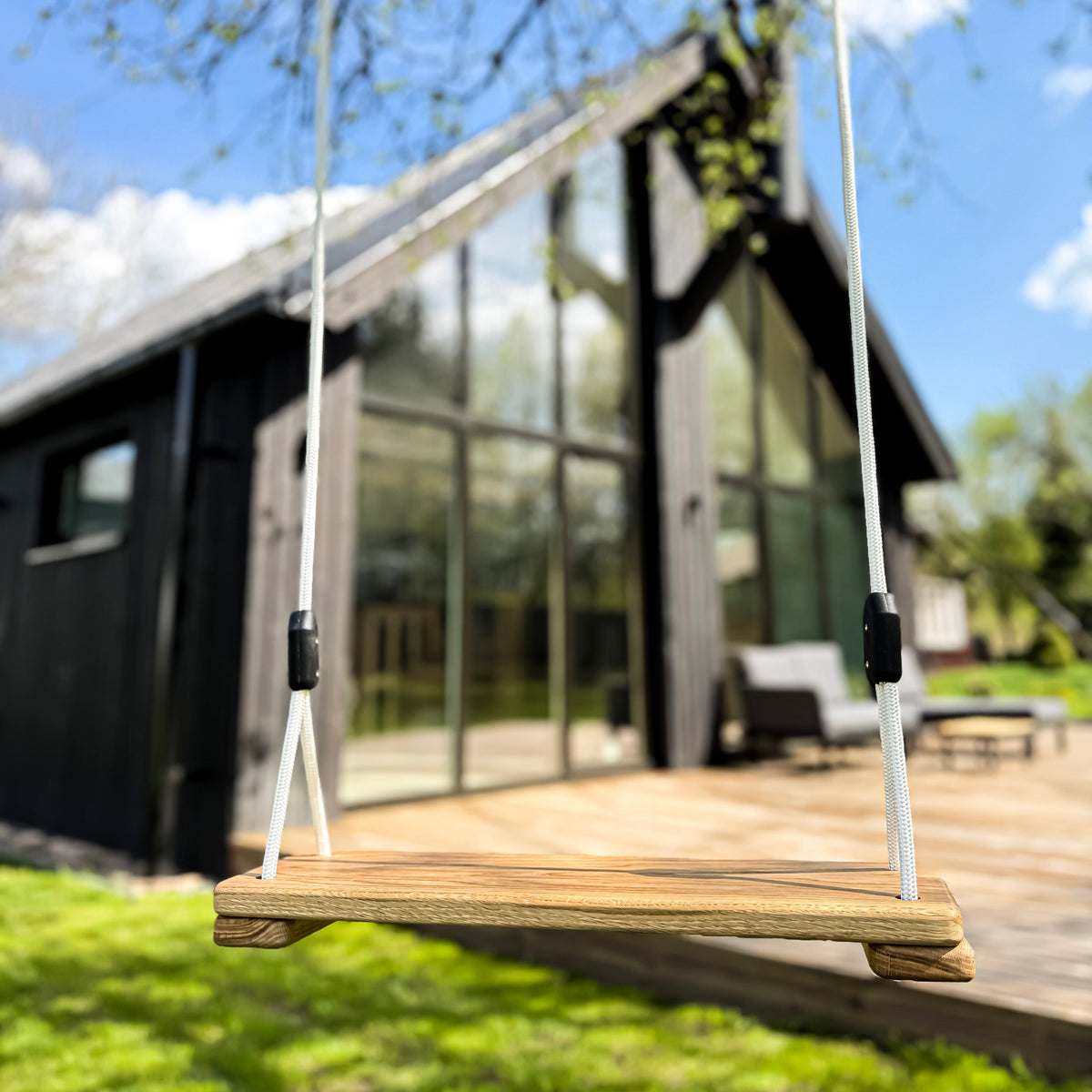 Wooden swing in front of a modern house with large glass windows.