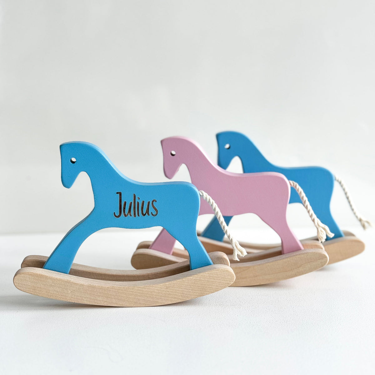 Two wooden rocking horses, one blue and one pink, on a white background.