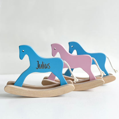 Two wooden rocking horses, one blue and one pink, on a white background.