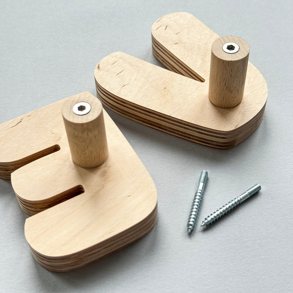 Two light natural wood letter-shaped peg toys with cylindrical pegs and two silver screws, arranged on a light gray background.