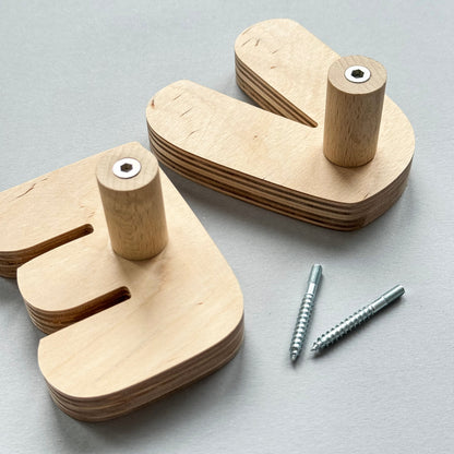 Two light natural wood letter-shaped peg toys with cylindrical pegs and two silver screws, arranged on a light gray background.