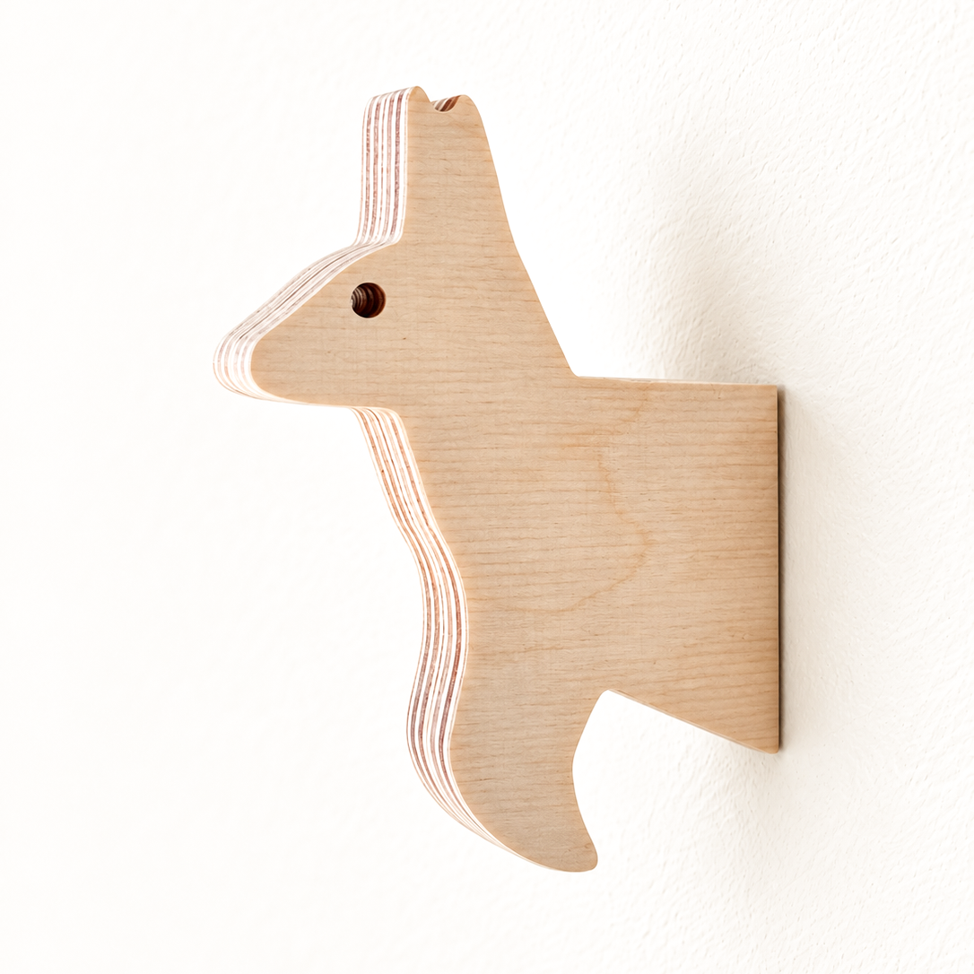 A minimalist wooden wall hook shaped like a kangaroo, made from layered light natural wood, mounted on a textured white wall.